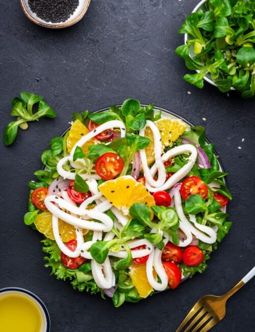 Fresh salad with squid, oranges, cherry tomatoes, lamb lettuce and olive oil with lemon juice